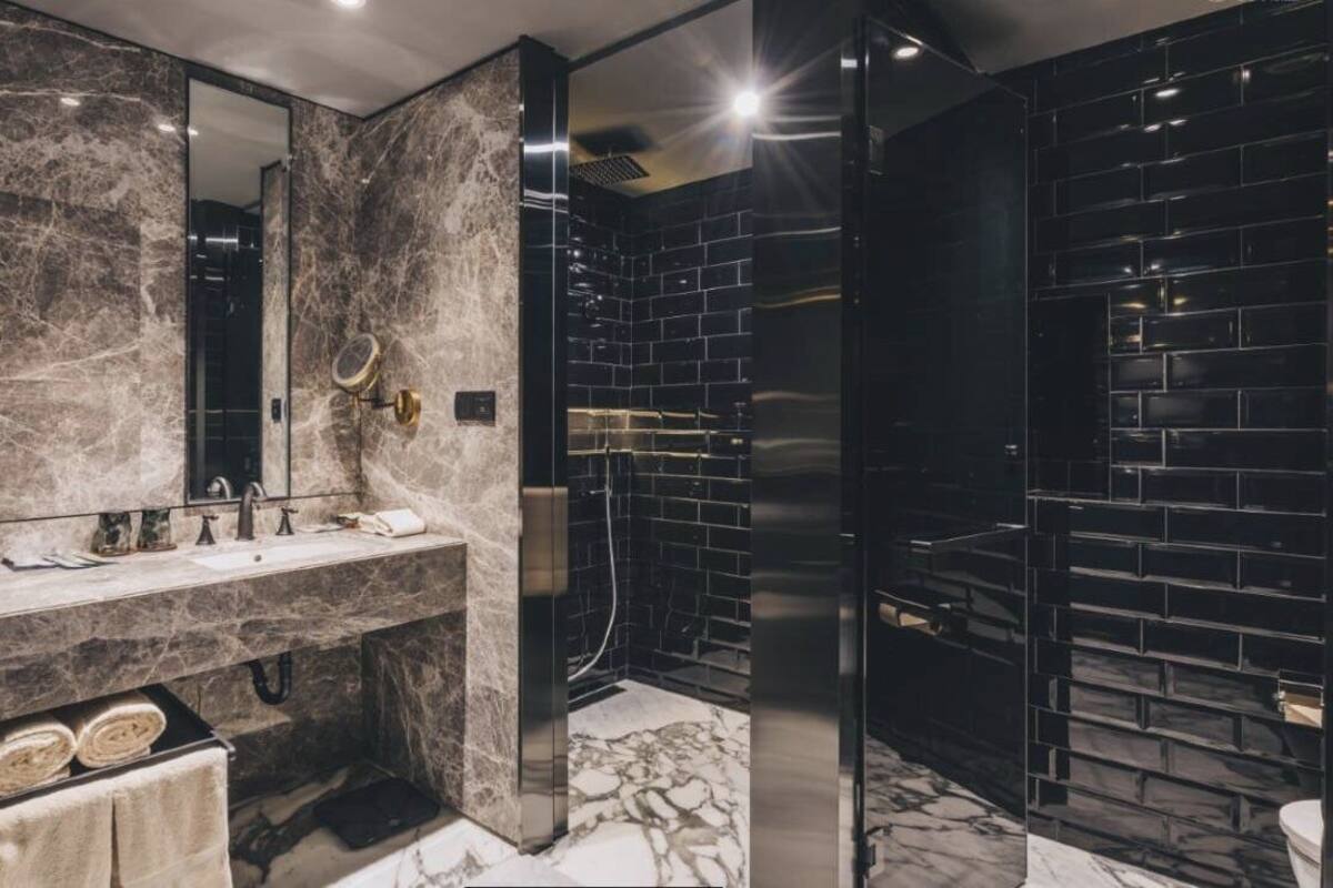 A modern bathroom with a marble vanity, a large mirror, and a black-tiled shower area.
