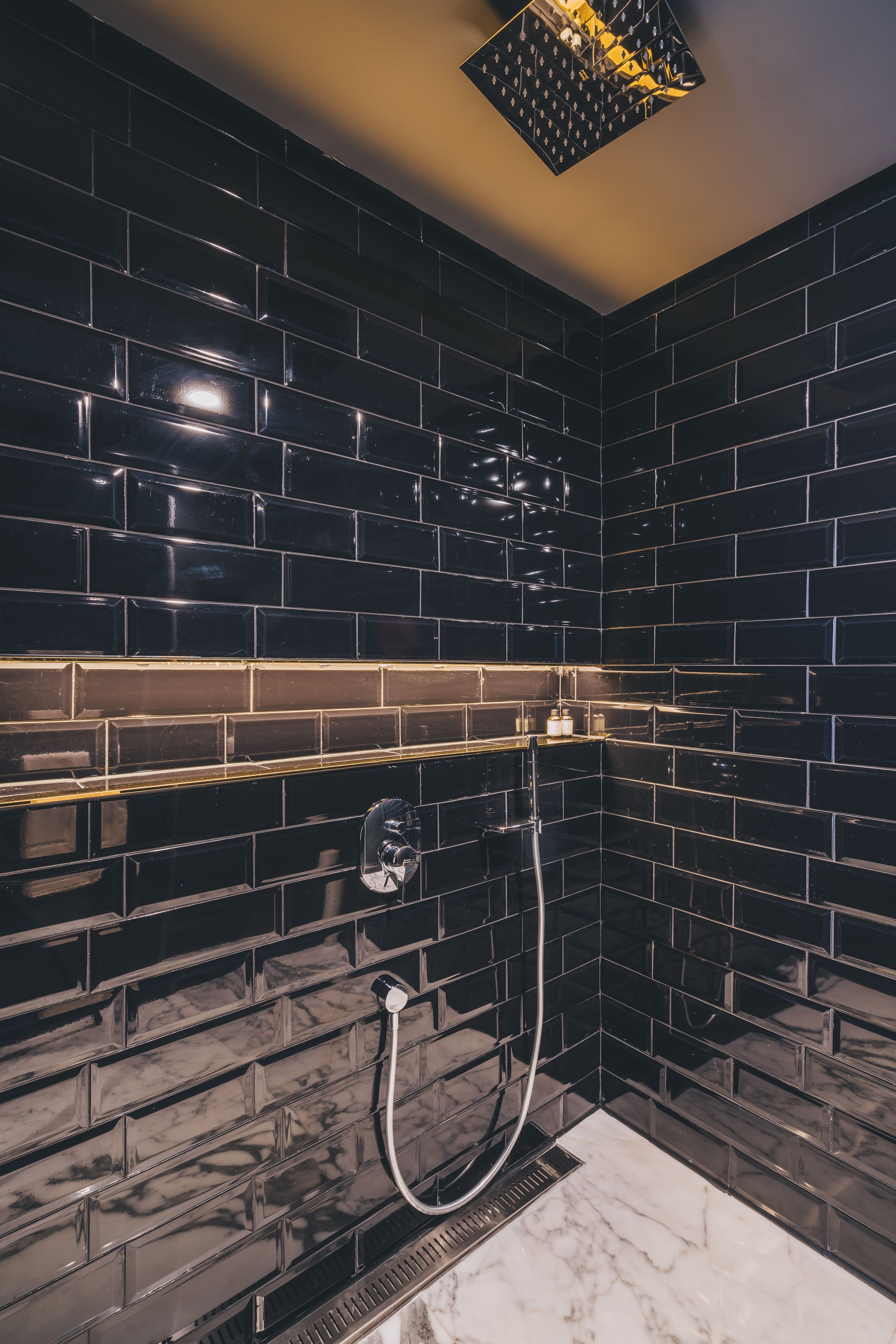 Ein modernes Badezimmer mit schwarzen Fliesenwänden, einem Marmorboden und einer ungewöhnlichen geometrischen Leuchte.