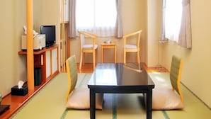 A room with a tatami mat floor, a wooden table, two chairs, a television on a stand, and a window with curtains.