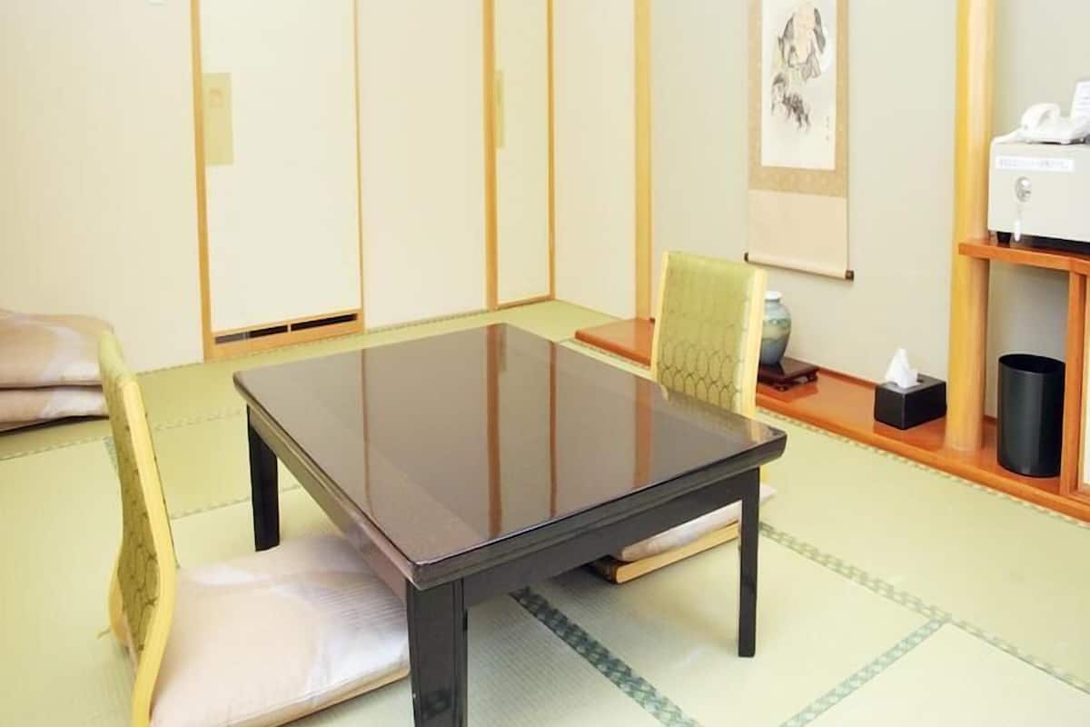 Um quarto tradicional japonês com tatames, uma mesa baixa, uma cadeira estofada e um portas correderas.