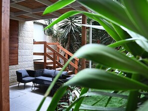 A covered outdoor seating area with a wooden staircase, stone walls, and lush greenery. - Carmella Spa & Boutique Hotel (Haifa)