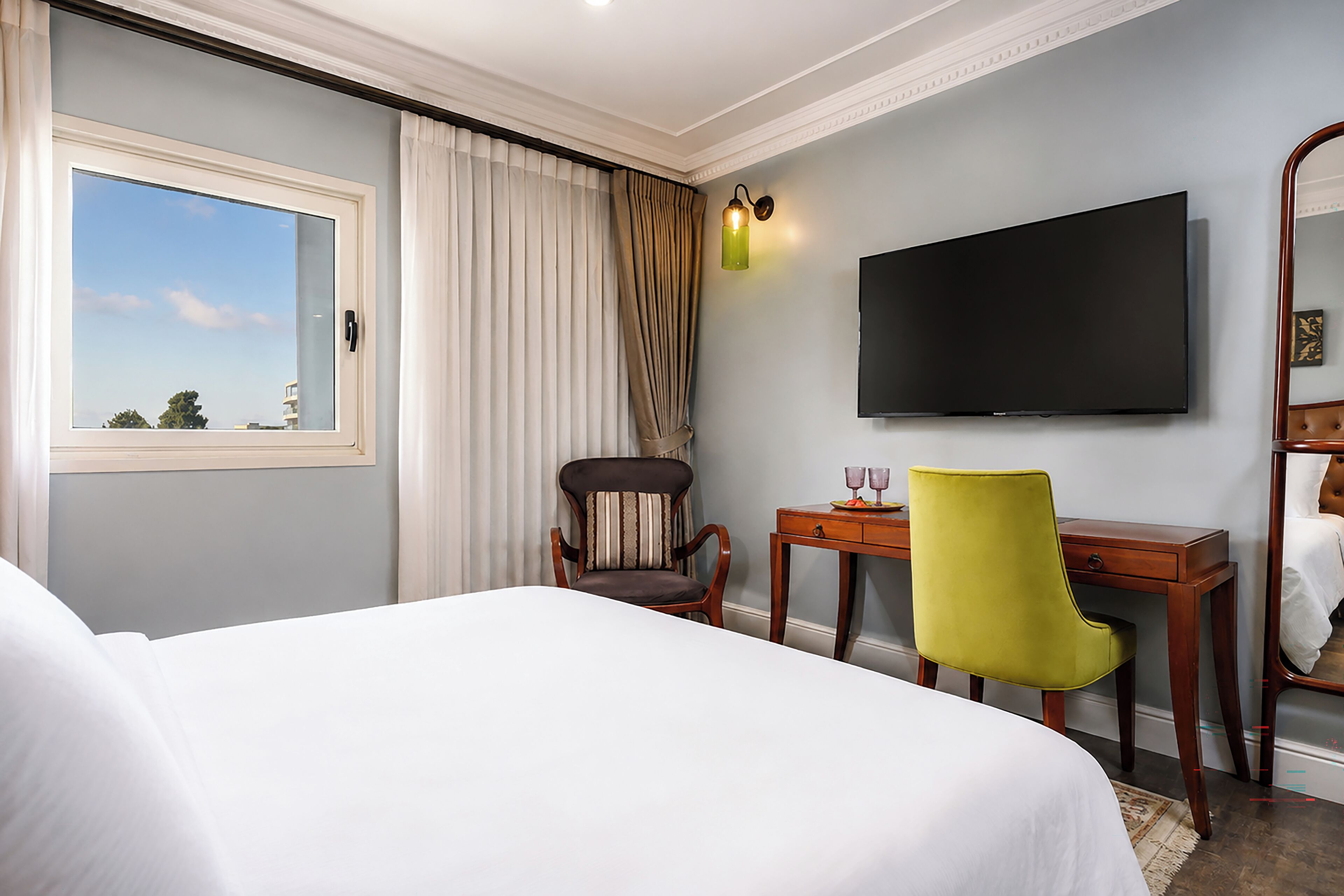 A hotel room with a bed, a desk, a chair, a television, and a window with curtains.