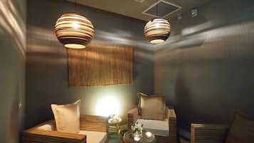 A modern room with two wooden sofas, a small round table with candles, and two hanging pendant lights.
