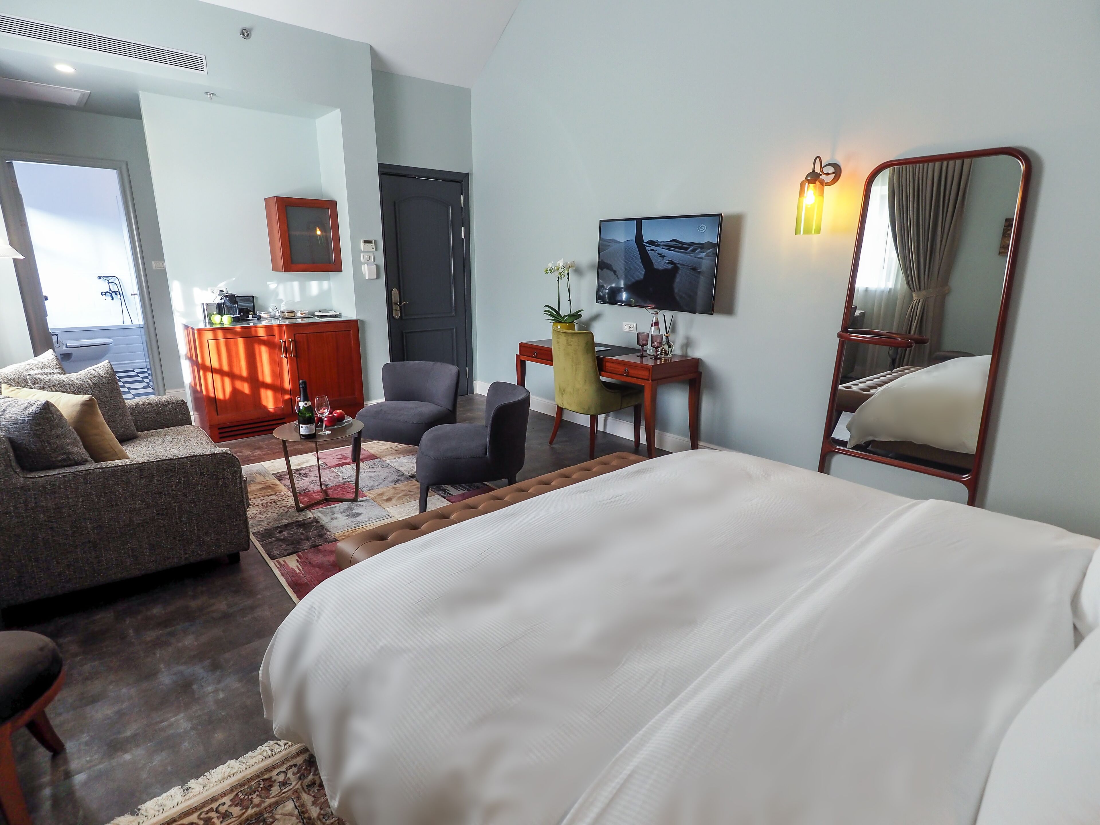 A hotel room with a bed, a sofa, a desk, a chair, and a view of the outdoors.