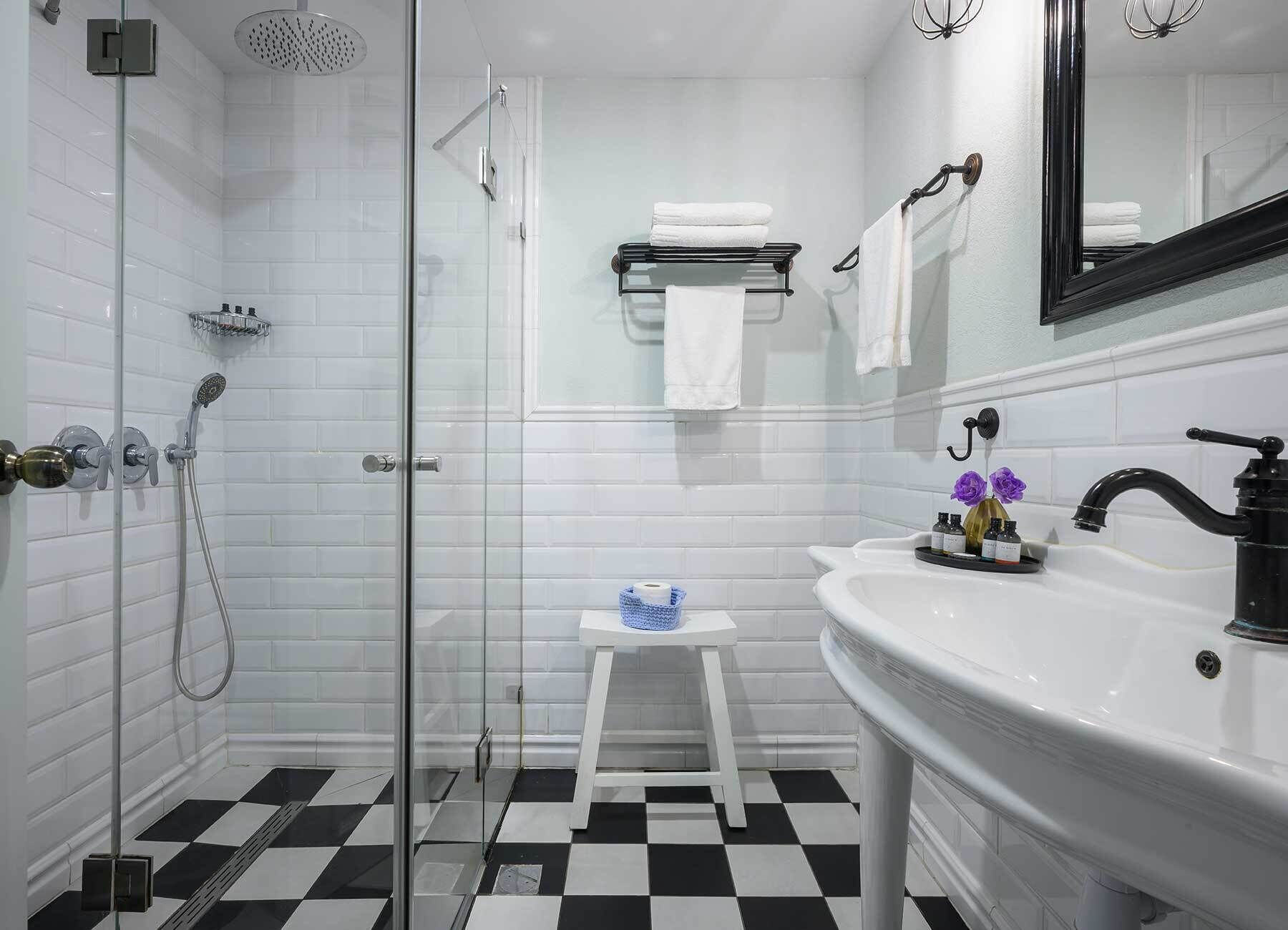 A bathroom with a glass shower enclosure, a white sink with a mirror, and a checkered floor.