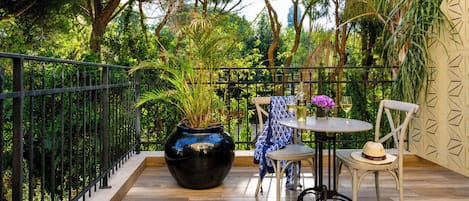 A balcony with a wooden floor, metal railing, a round table with chairs, a vase with flowers, and a potted plant.