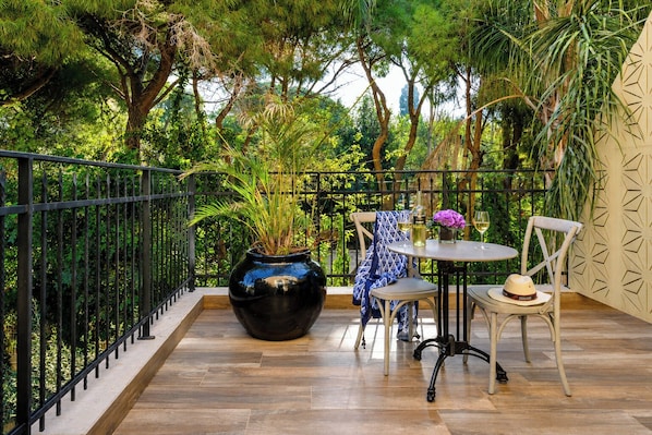 A balcony with a wooden floor, metal railing, a round table with chairs, a vase with flowers, and a potted plant. - Carmella Spa & Boutique Hotel (Haifa)
