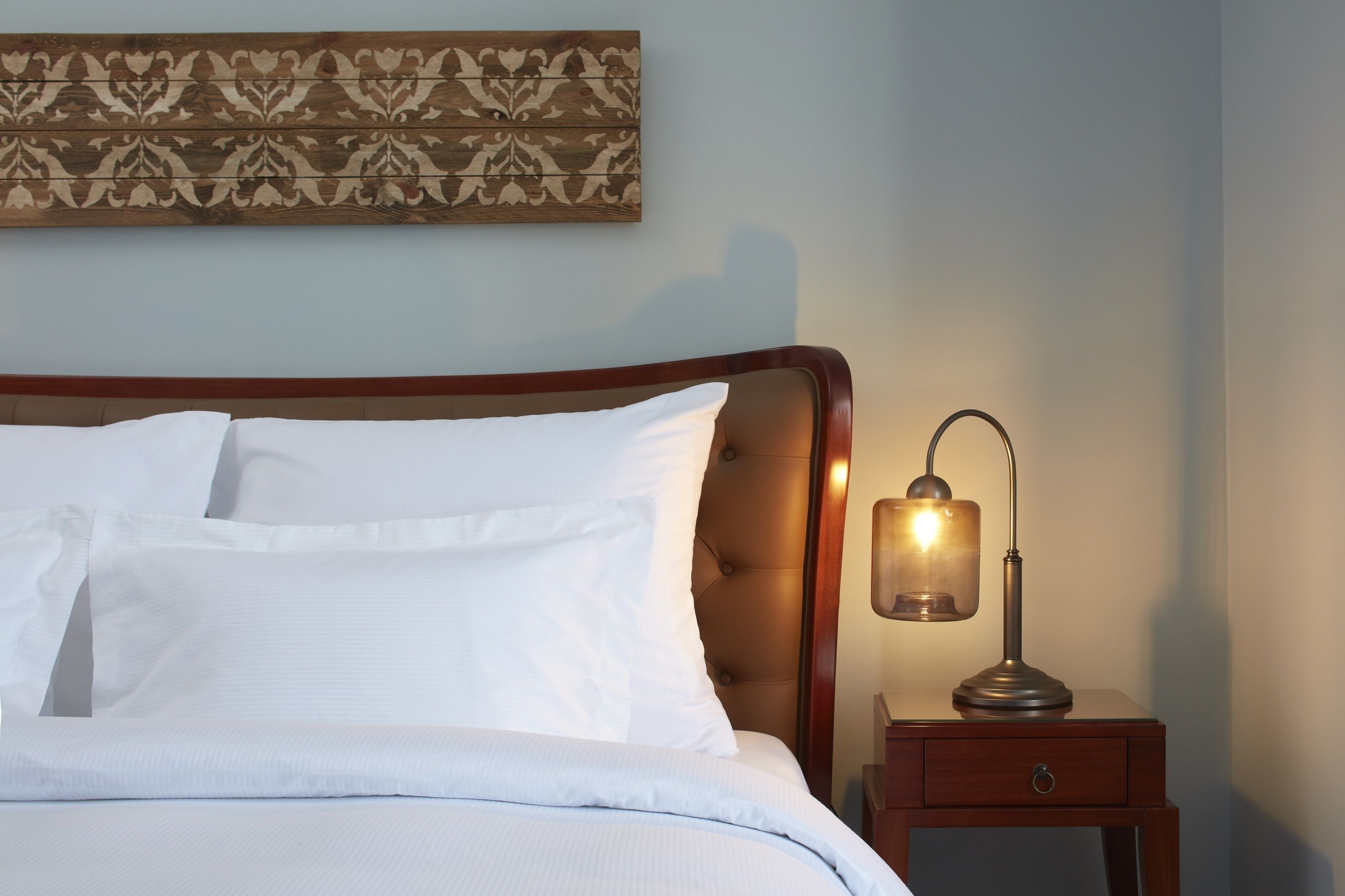A neatly made bed with white linens, a wooden headboard, and a bedside table with a lamp.