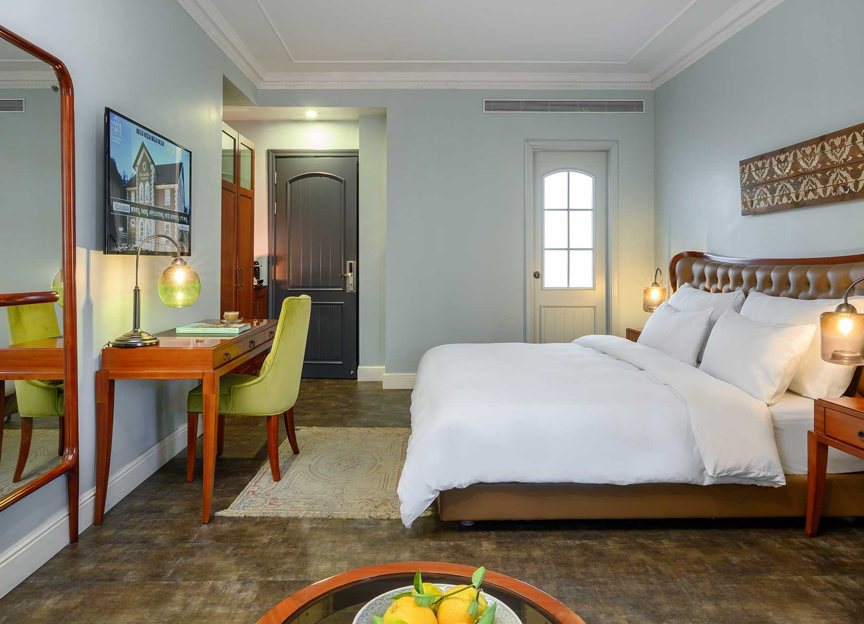 A hotel room with a bed, desk, chair, and a small table with fruit.