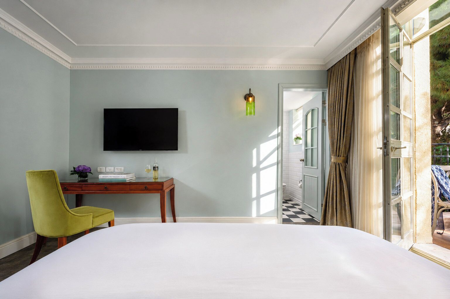 Habitación de hotel con una cama grande, un escritorio con una silla, un televisor de pantalla plana y vistas al exterior.