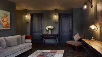 Una sala de estar con un sofá, una silla, una mesita y un jarrón decorativo con flores. Se observan dos puertas con los números 403 y 404, y una lámpara fijada a la pared.