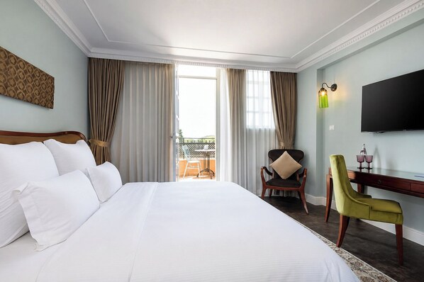 A hotel room with a large bed, a desk with a chair, a television, and a balcony with curtains. - Carmella Spa & Boutique Hotel (Haifa)
