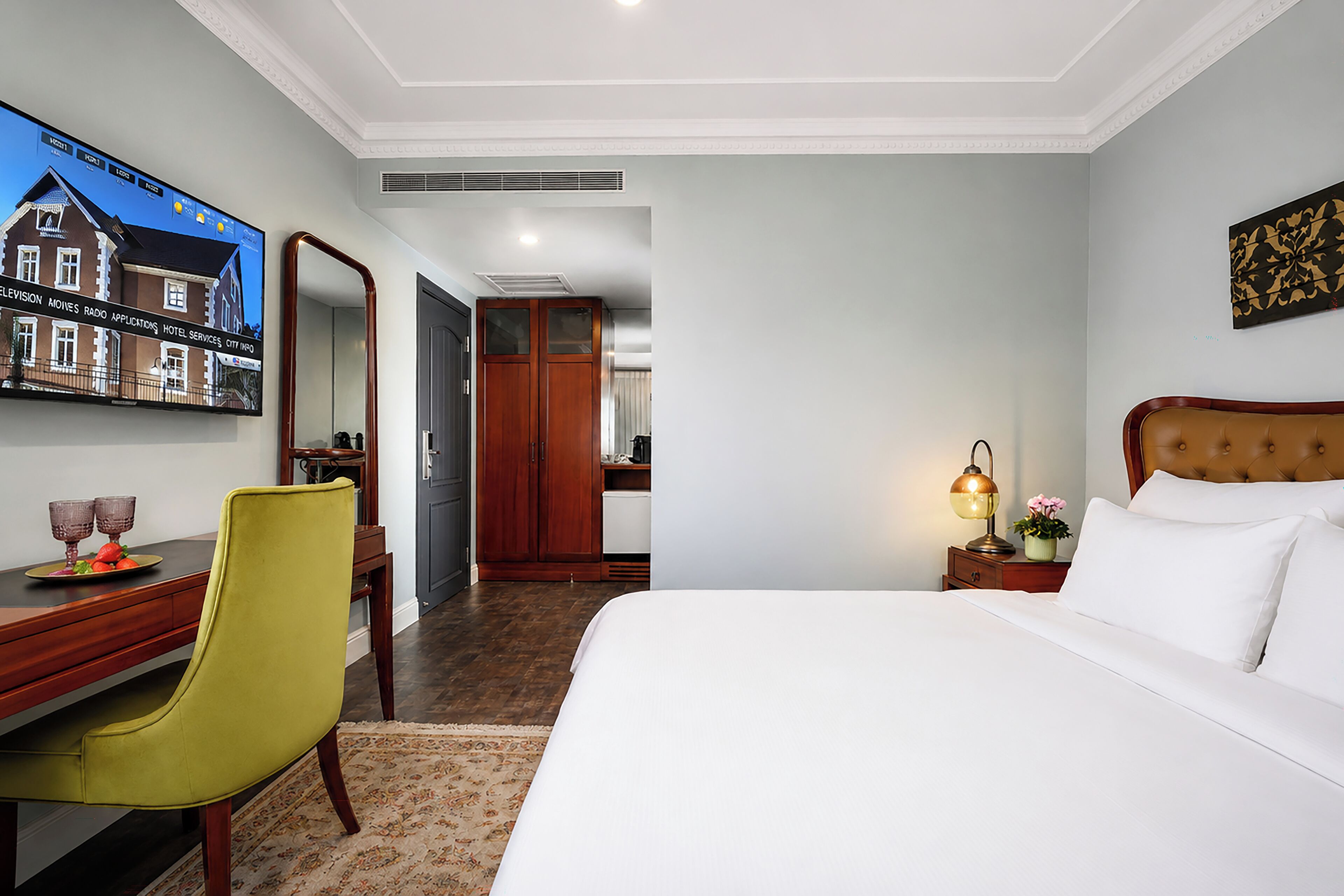 A hotel room with a bed, a desk with a chair, a TV, and a nightstand with a lamp.