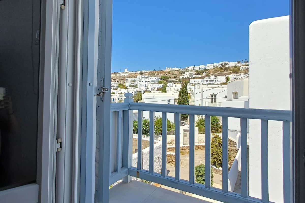A balcony with a white railing, a clear blue sky, and a view of white buildings in the distance.