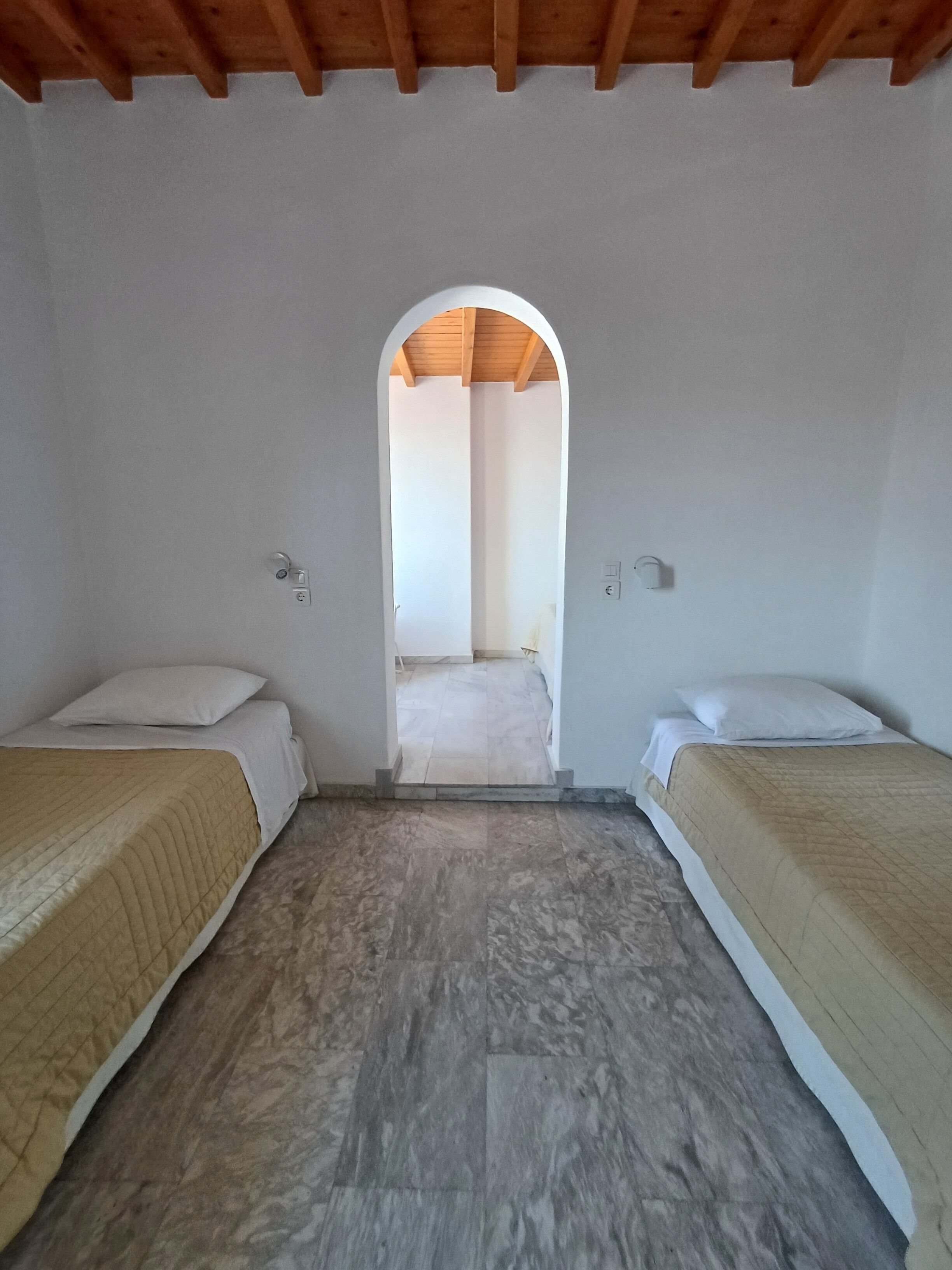 A room with two beds, a wooden ceiling, and a tiled floor.