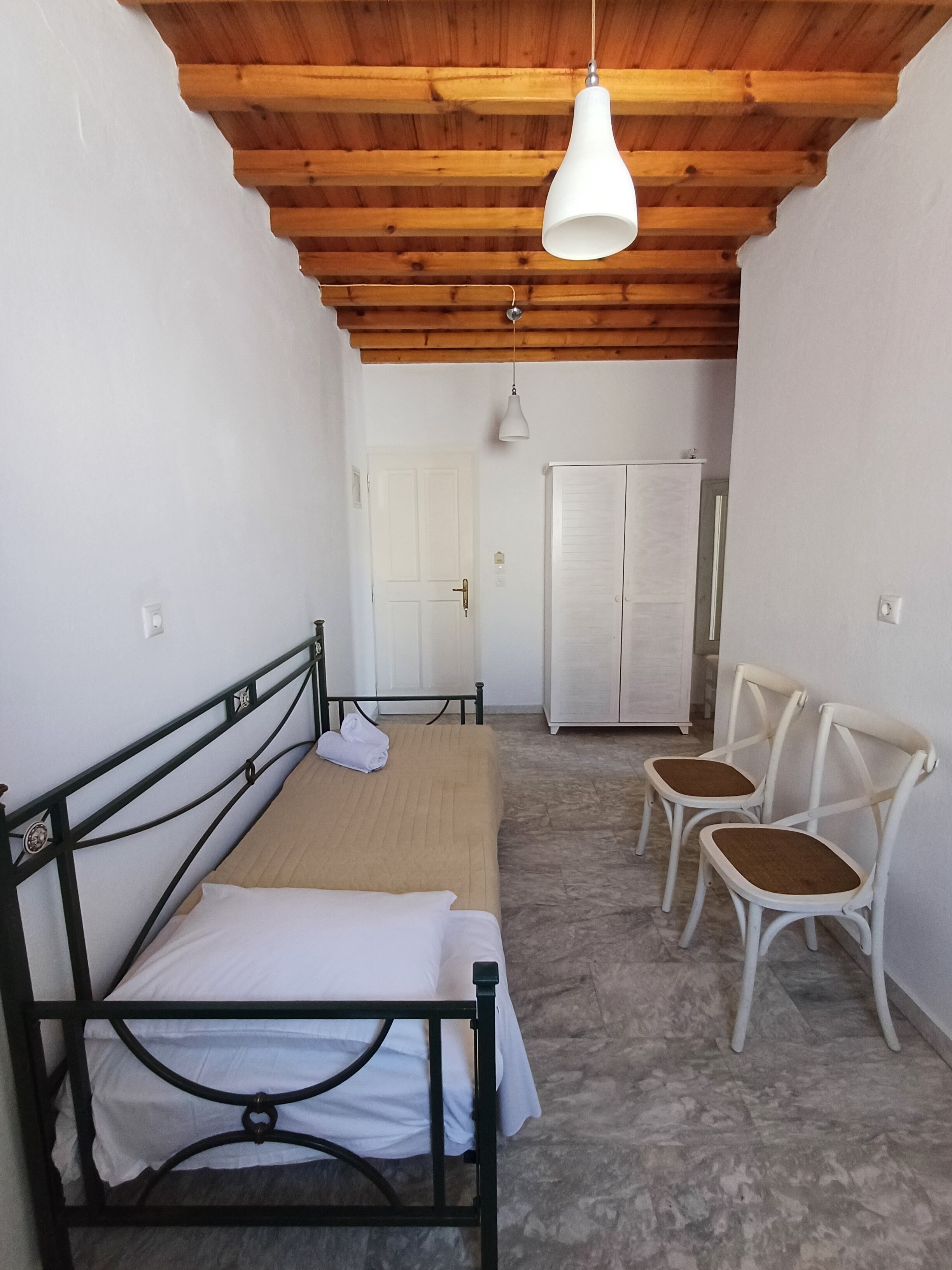 A bedroom with a bed, two chairs, a wardrobe, and a hanging light fixture.