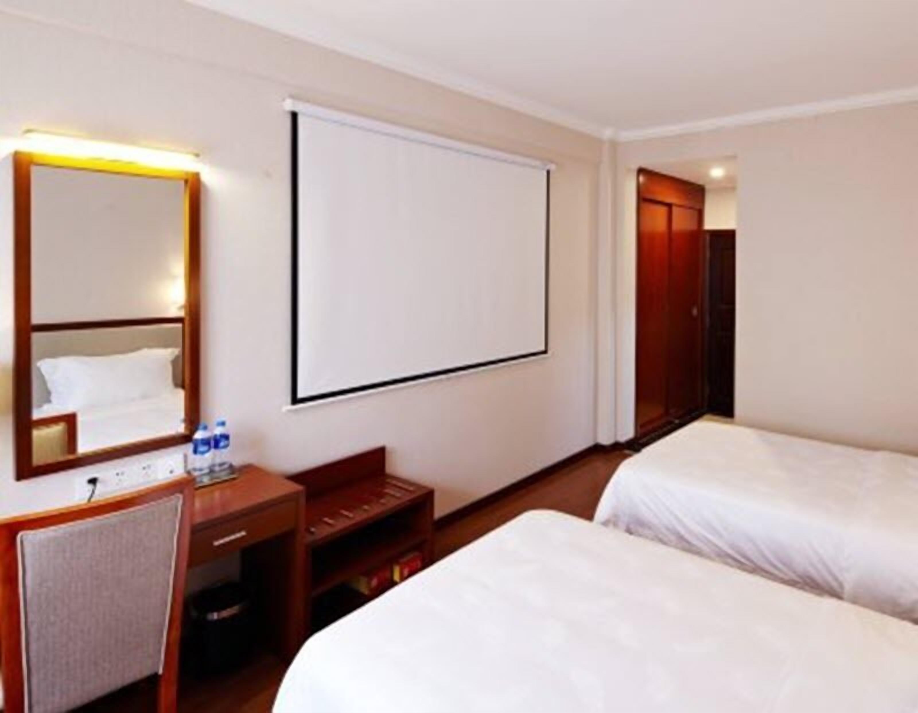 Ein Hotelzimmer mit zwei Betten, einem Schreibtisch mit Stuhl, einem Spiegel, einem Fernseher und einem Kleiderschrank.