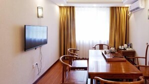 Un salón de conferencias con una larga mesa de madera, varias sillas, un televisor de pantalla plana en la pared y un ventanal con cortinas.