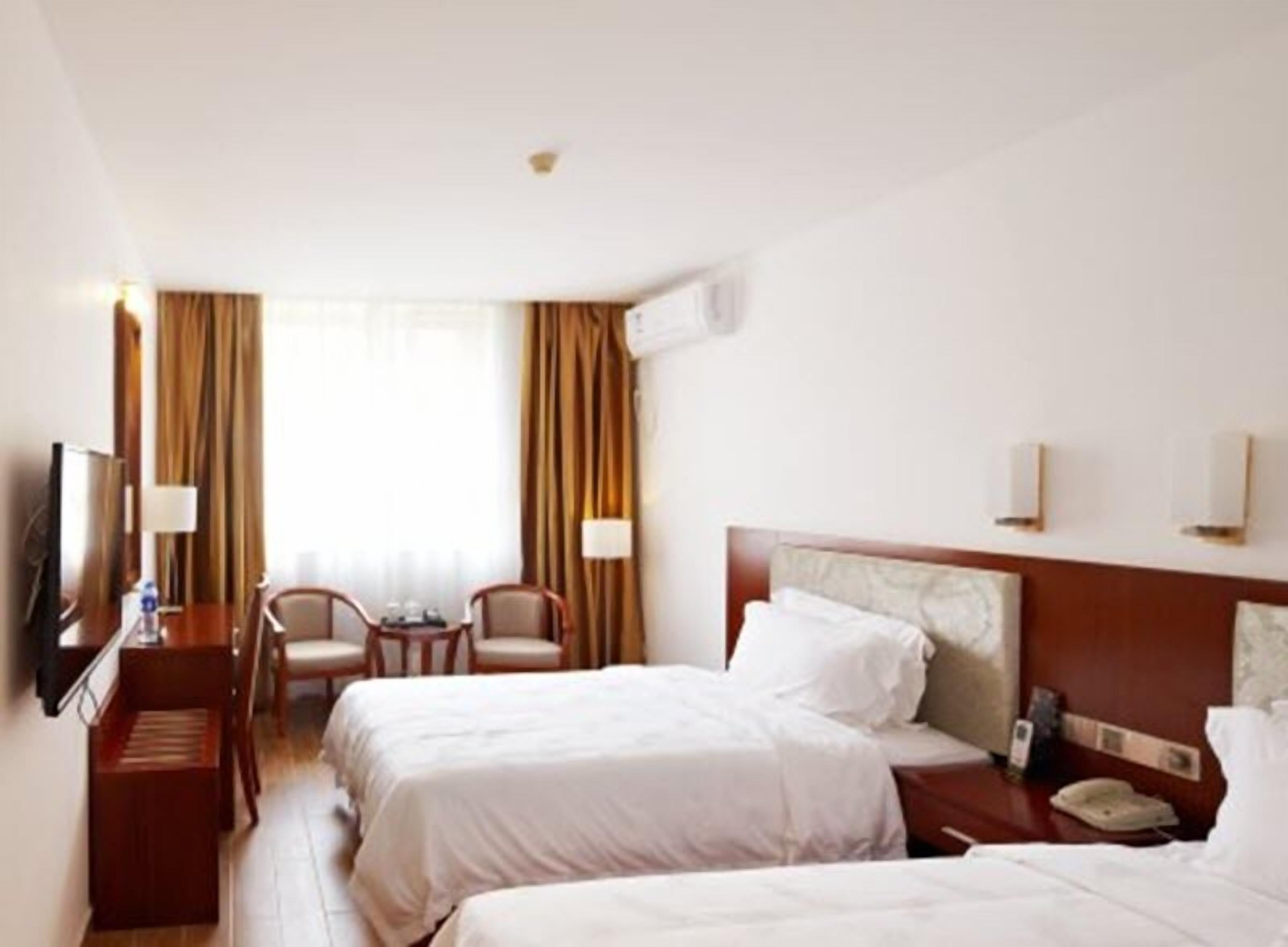 A hotel room with two beds, a desk with a chair, a TV, and a window with curtains.