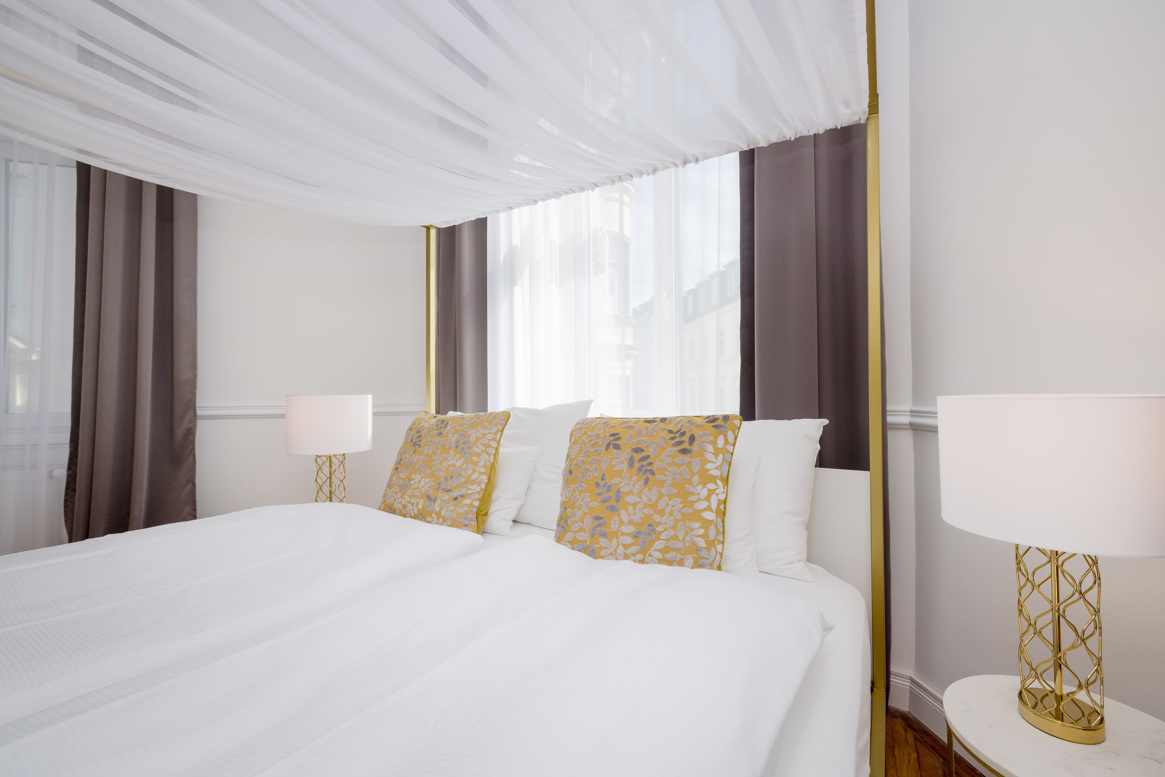 A hotel room with a large bed, two bedside tables with lamps, and a view of the city through the window.