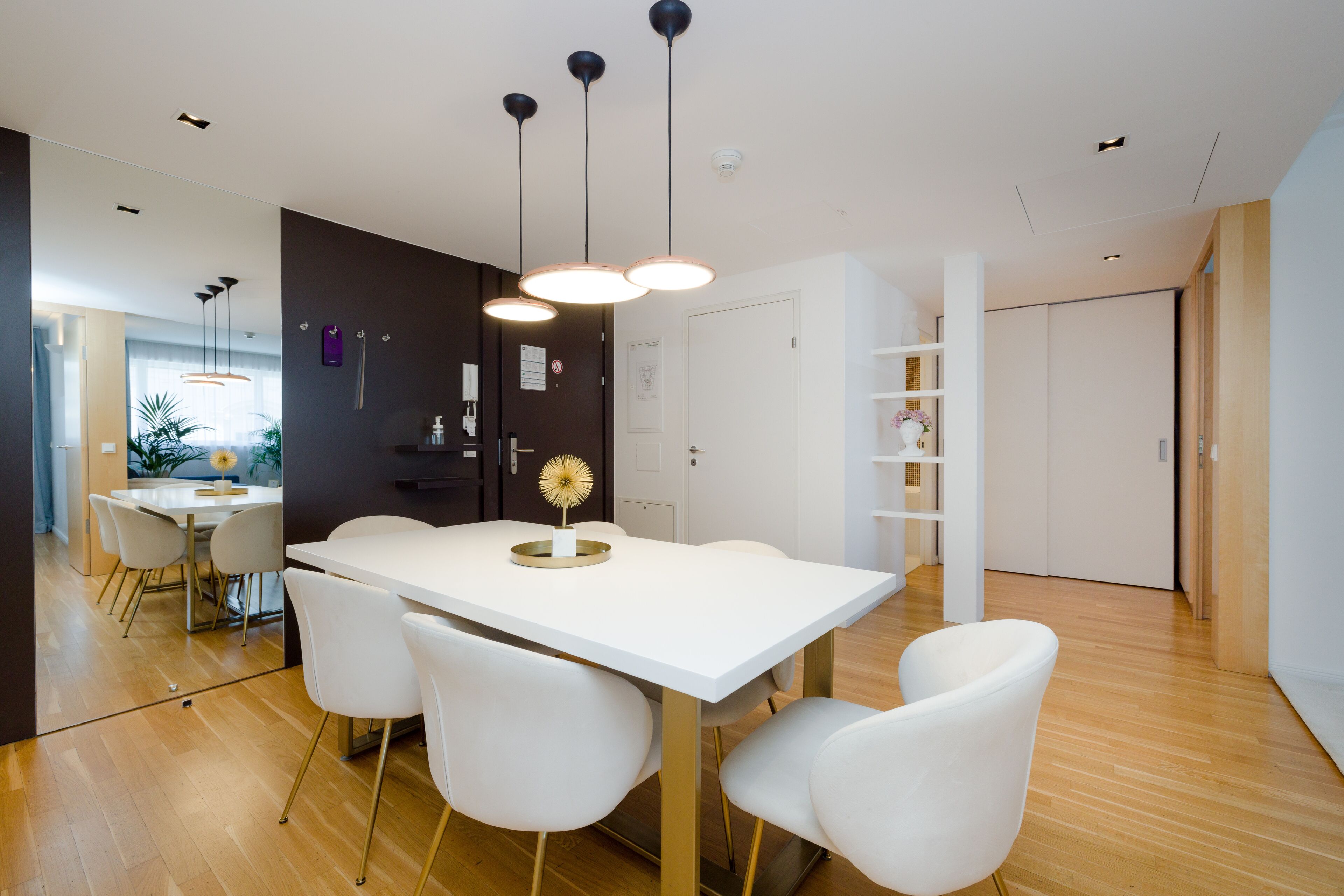 A modern dining area with a white table, four white chairs, and pendant lighting.