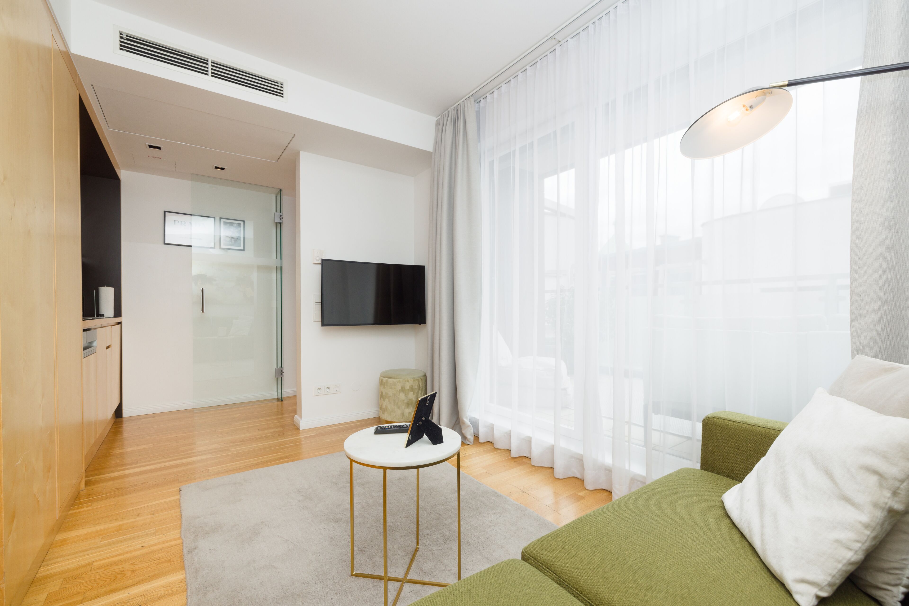A modern living room with a green sofa, a small white table, and a flat-screen TV mounted on the wall.