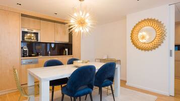 A modern kitchen with wooden cabinets, a built-in oven, and a dining area with a white table and blue chairs.