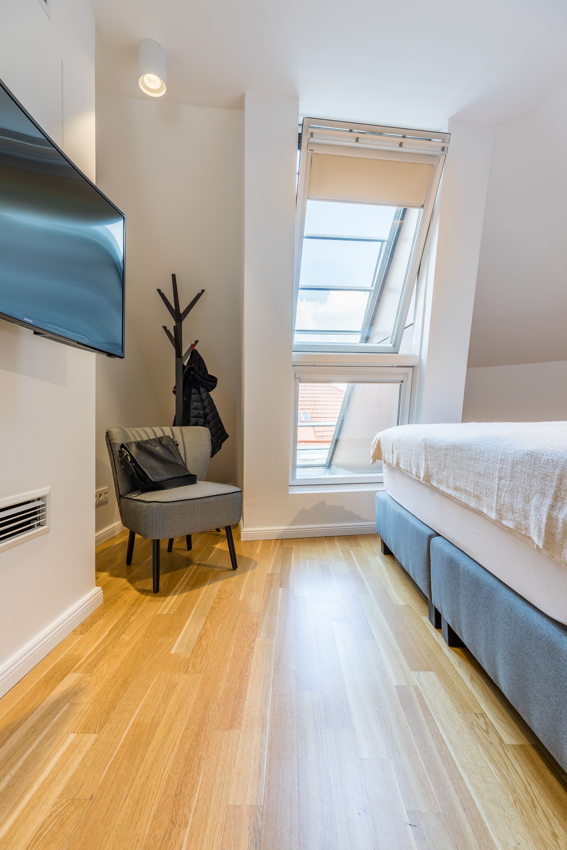 A compact bedroom with a skylight, a flat-screen TV, a chair with a bag, and a bed.
