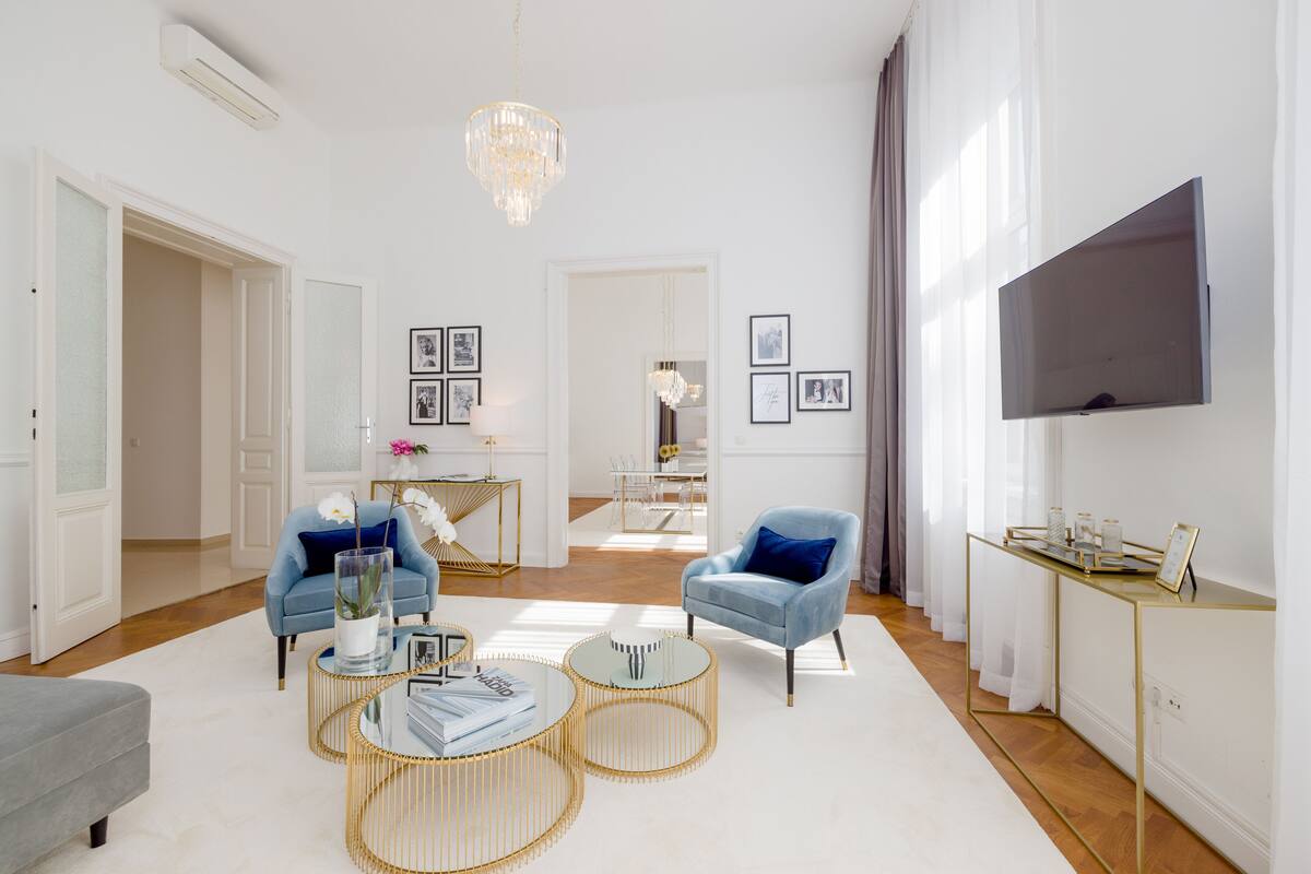 Un soggiorno moderno con un lampadario, due poltrone, un tavolino da caffè e un televisore a schermo piatto montato a parete.