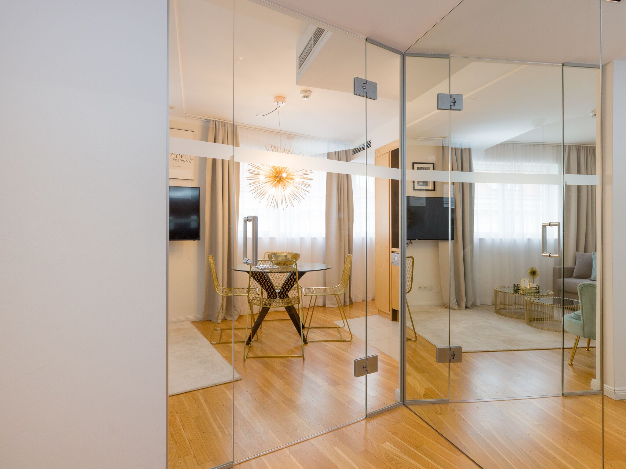 Ein modernes Zimmer mit Glastrennwand, einem Essbereich mit Glastisch und Stühlen, einer Sitzecke und einem Fernseher.