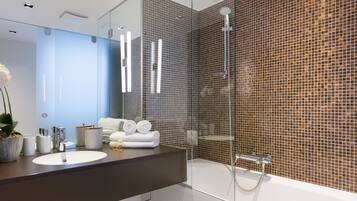 Un baño moderno con cabina de ducha de vidrio, un espejo grande y una encimera oscura con lavamanos y artículos de aseo.