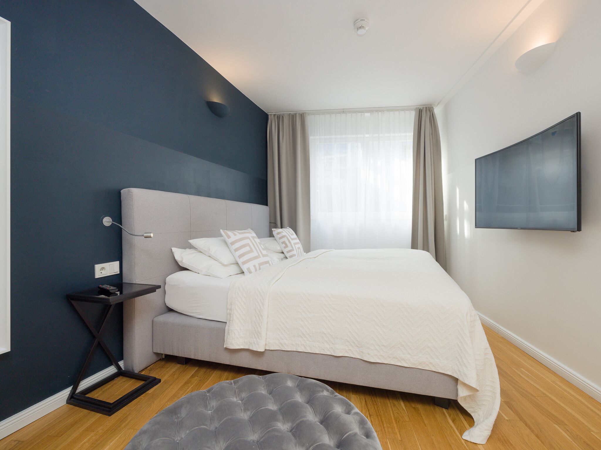 Ein modernes Schlafzimmer mit Bett, Nachttisch und einem an der Wand montierten Flachbildfernseher.
