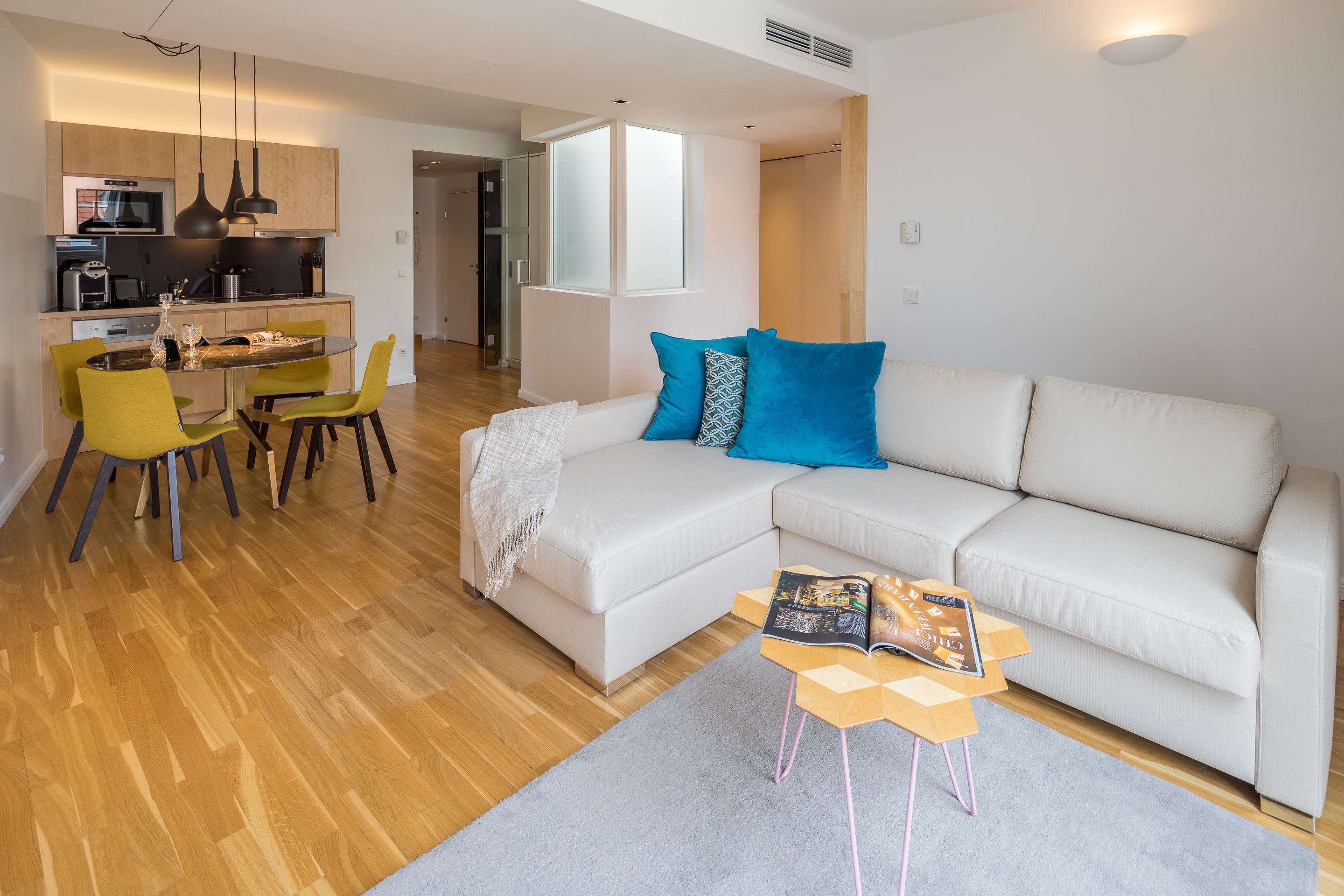 Una sala de estar moderna con un sofá blanco, una mesa de comedor con sillas y una cocina al fondo.