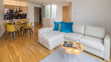 Una sala de estar moderna con un sofá blanco, una mesa de comedor con sillas y una cocina al fondo.