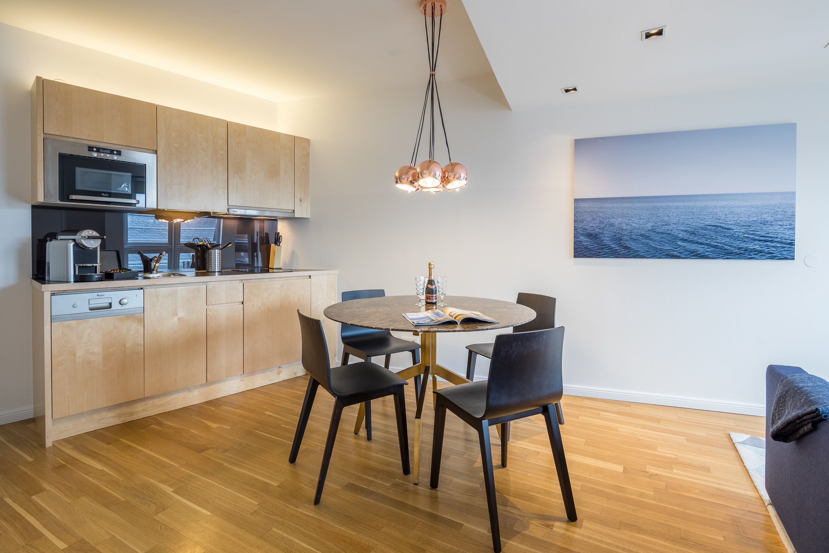 A modern kitchen with wooden cabinets, a built-in oven, and a dining area with a round table and chairs.