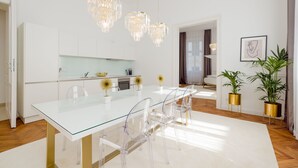A modern kitchen with white cabinets, a glass dining table, and gold accents. - Rafael Kaiser - Premium Apartments City Centre  (Vienna)