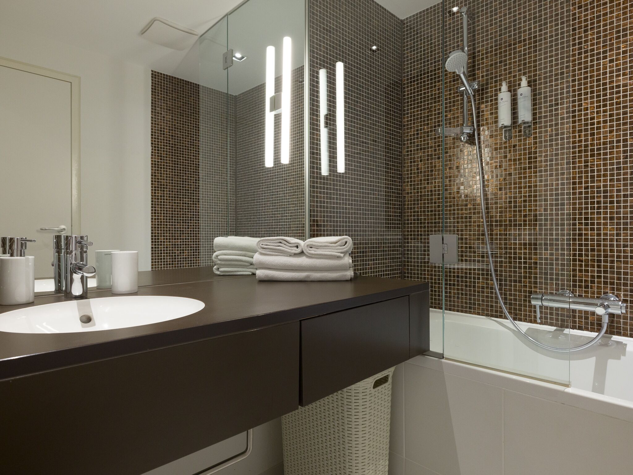 A modern bathroom with a large mirror, a dark brown vanity, a white sink, and a glass-enclosed shower area.