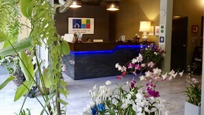 A hotel reception desk with a blue accent, surrounded by potted orchids and a sign reading "The Beach Cha-Am Guest House". - The Beach Cha Am Residence (Cha-am)