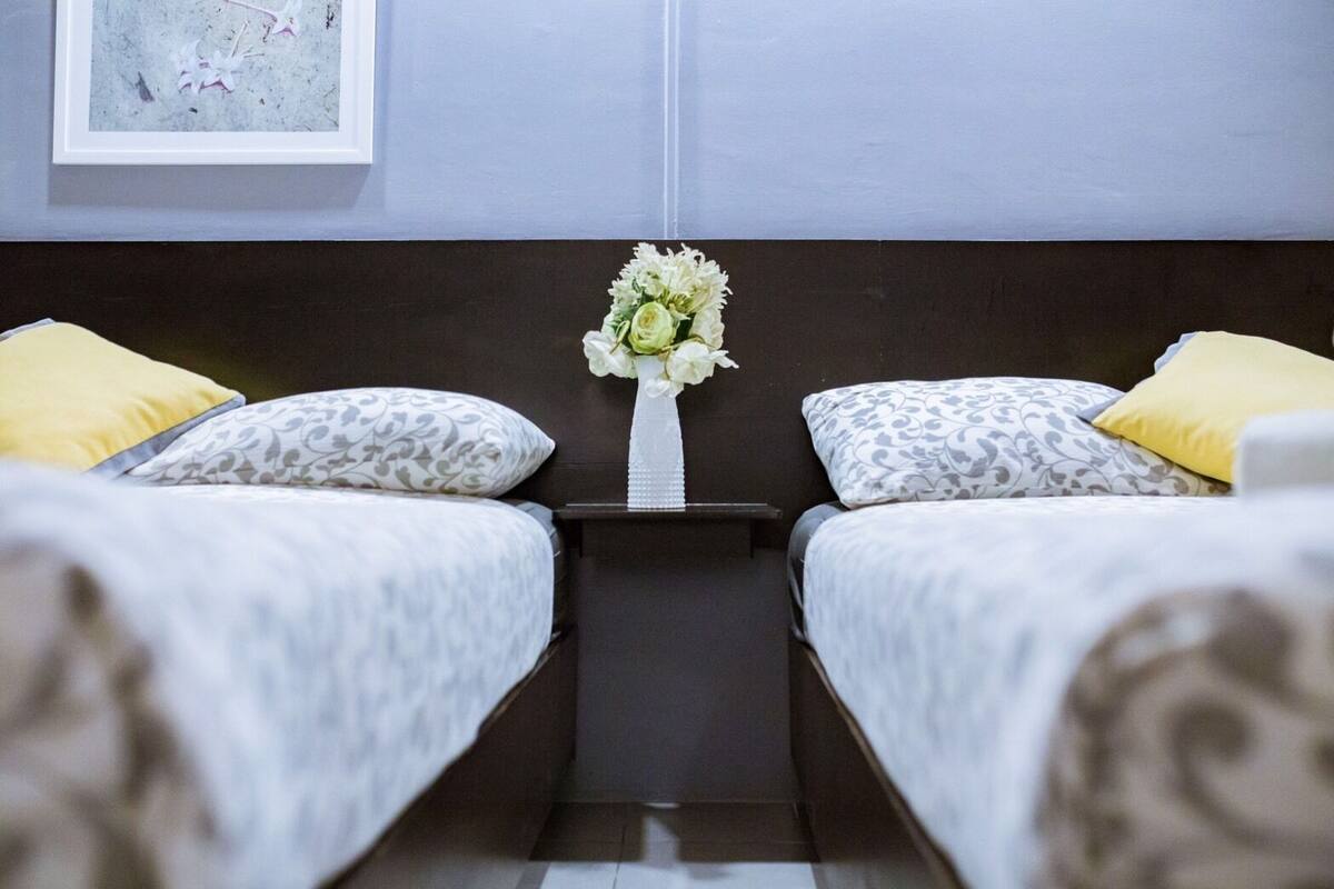 Une chambre d’hôtel avec deux lits, chacun agrémenté de draps à motifs, une table de chevet avec un vase de fleurs et un tableau encadré au mur.