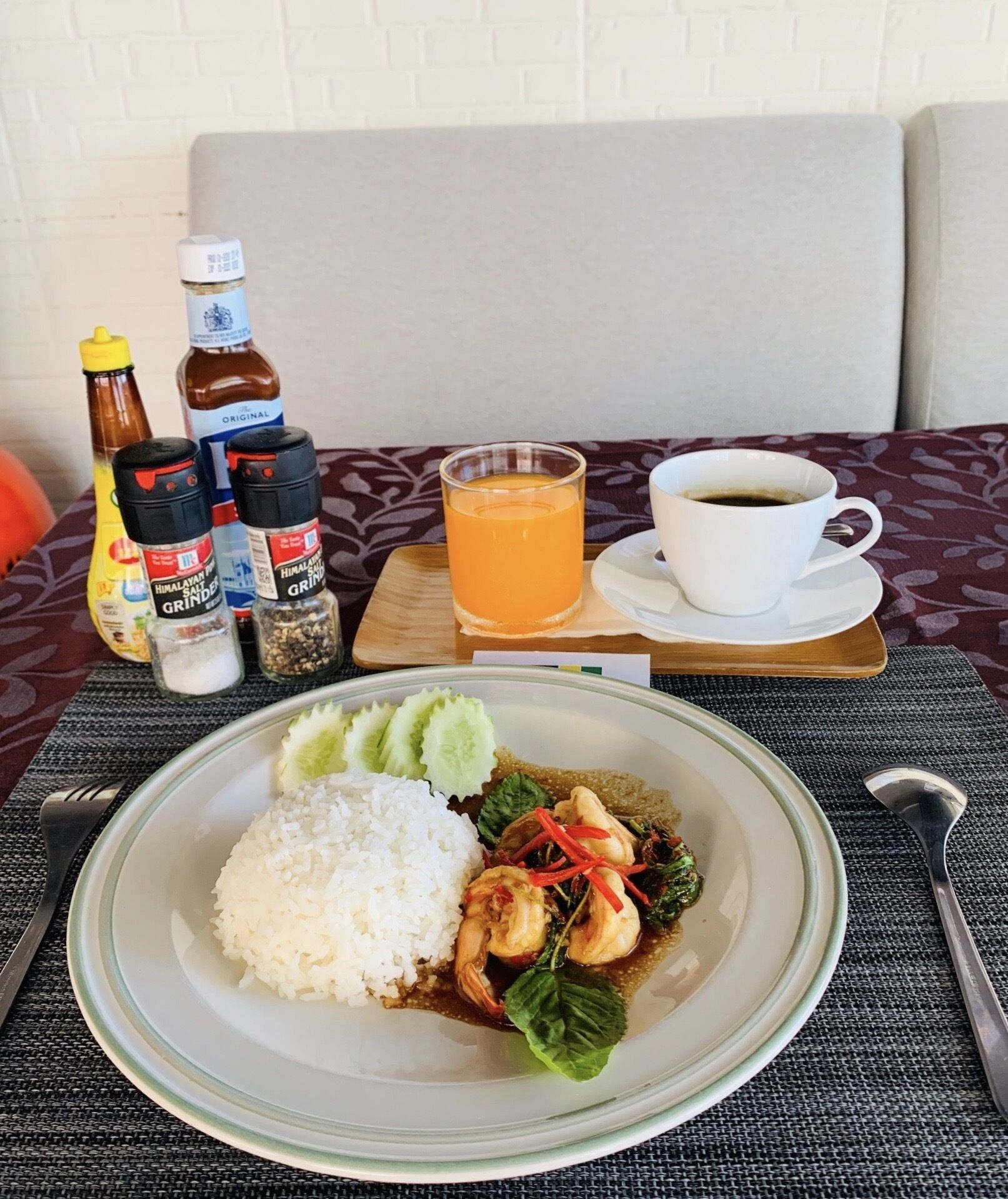 A meal with rice, shrimp, and vegetables, accompanied by condiments and a cup of coffee on a table.