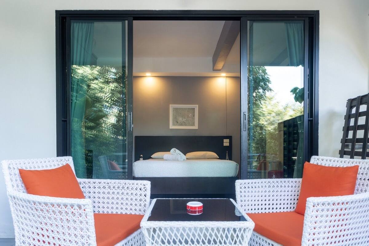Une chambre à coucher avec un lit, une table de chevet et deux fauteuils en osier dotés de coussins orange.