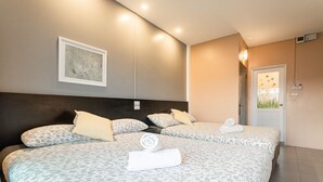 A hotel room with two beds, each with patterned bedding and pillows, a dark headboard, a framed artwork on the wall, and a door with a window view. - The Beach Cha Am Residence (Cha-am)