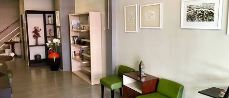 A modern living room with a green sofa, a wooden coffee table, and a bookshelf. There are framed pictures on the wall and a staircase leading to another room.