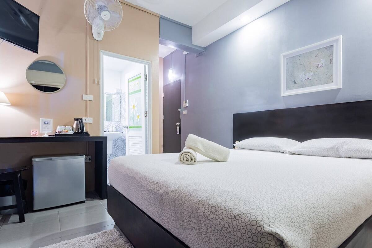 Une chambre d’hôtel avec un lit, un bureau équipé d’un ordinateur, un ventilateur et une porte donnant sur un balcon.