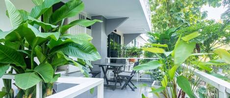 A balcony with a table and chairs, surrounded by large green plants.