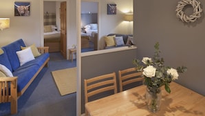 Una habitación acogedora con un sofá azul, una mesa de comedor de madera y un espejo que refleja otra habitación.