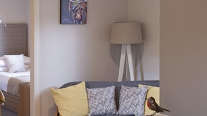 Habitación de hotel con cama, sofá con cojines estampados, lámpara y un cuadro en la pared.