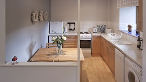 Una cocina compacta con una mesa de madera, un refrigerador, un horno, un lavamanos y una lavadora.