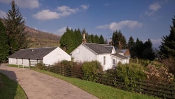 A rural property with a gravel driveway leading to a white building with a fenced yard.