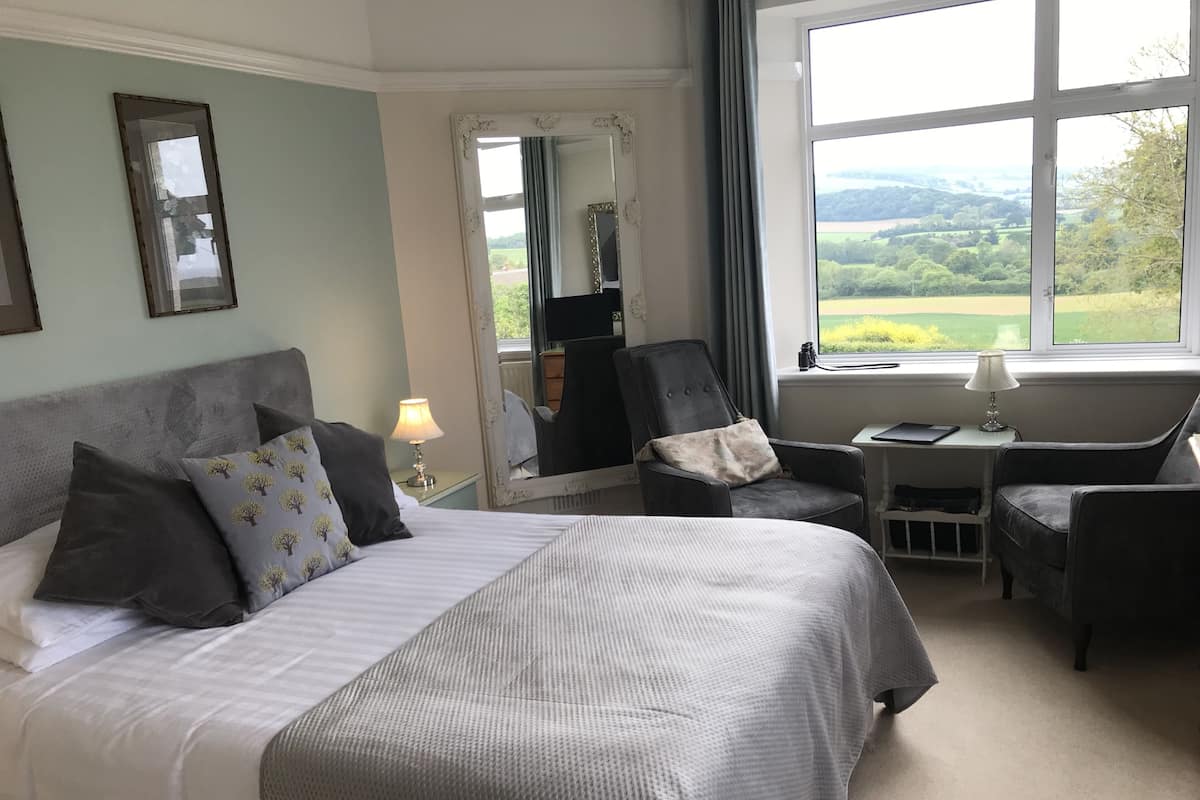Une chambre d’hôtel avec un grand lit, un bureau, une chaise et une vue sur la campagne.